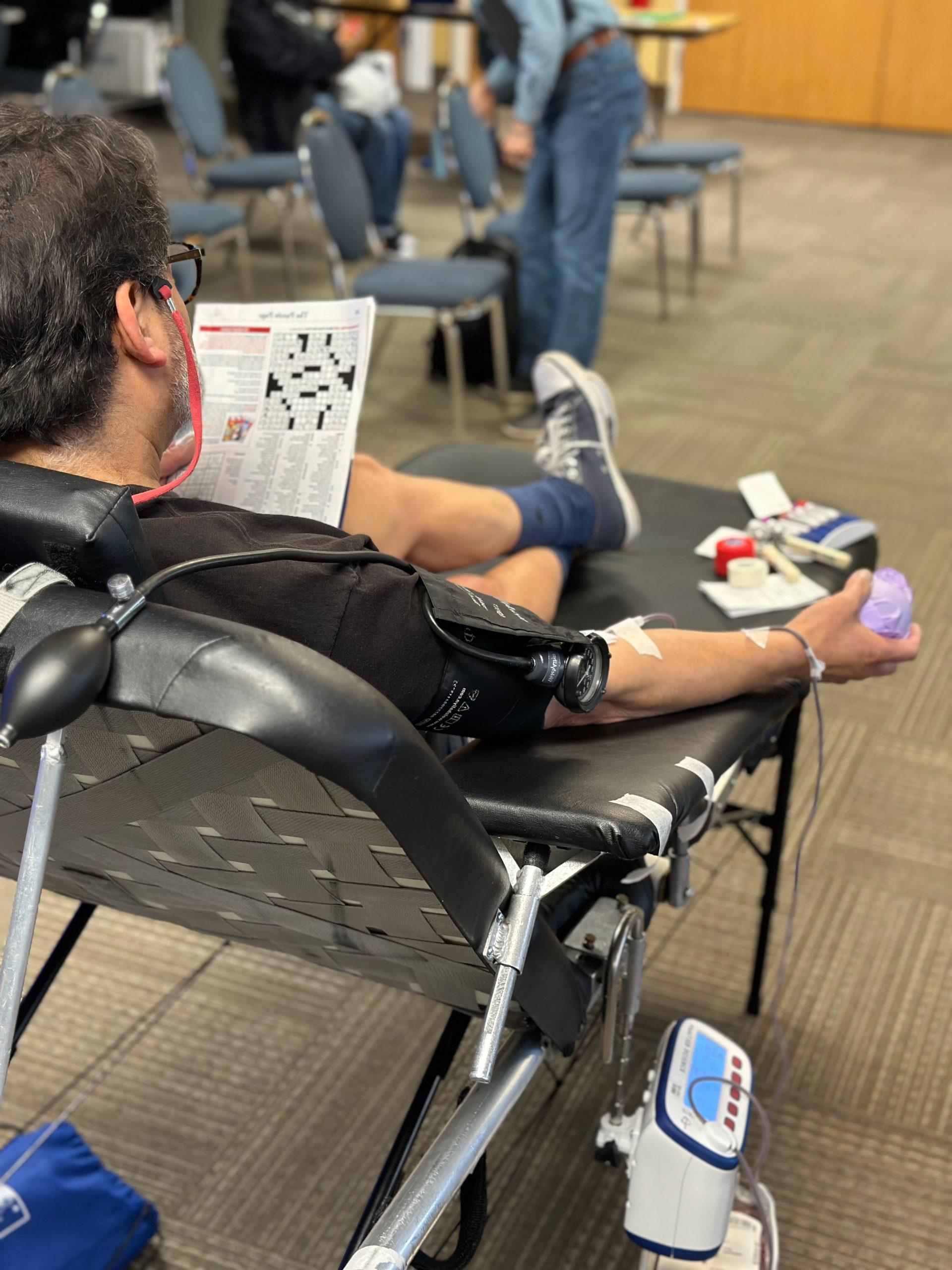 man giving blood and reading cross word.